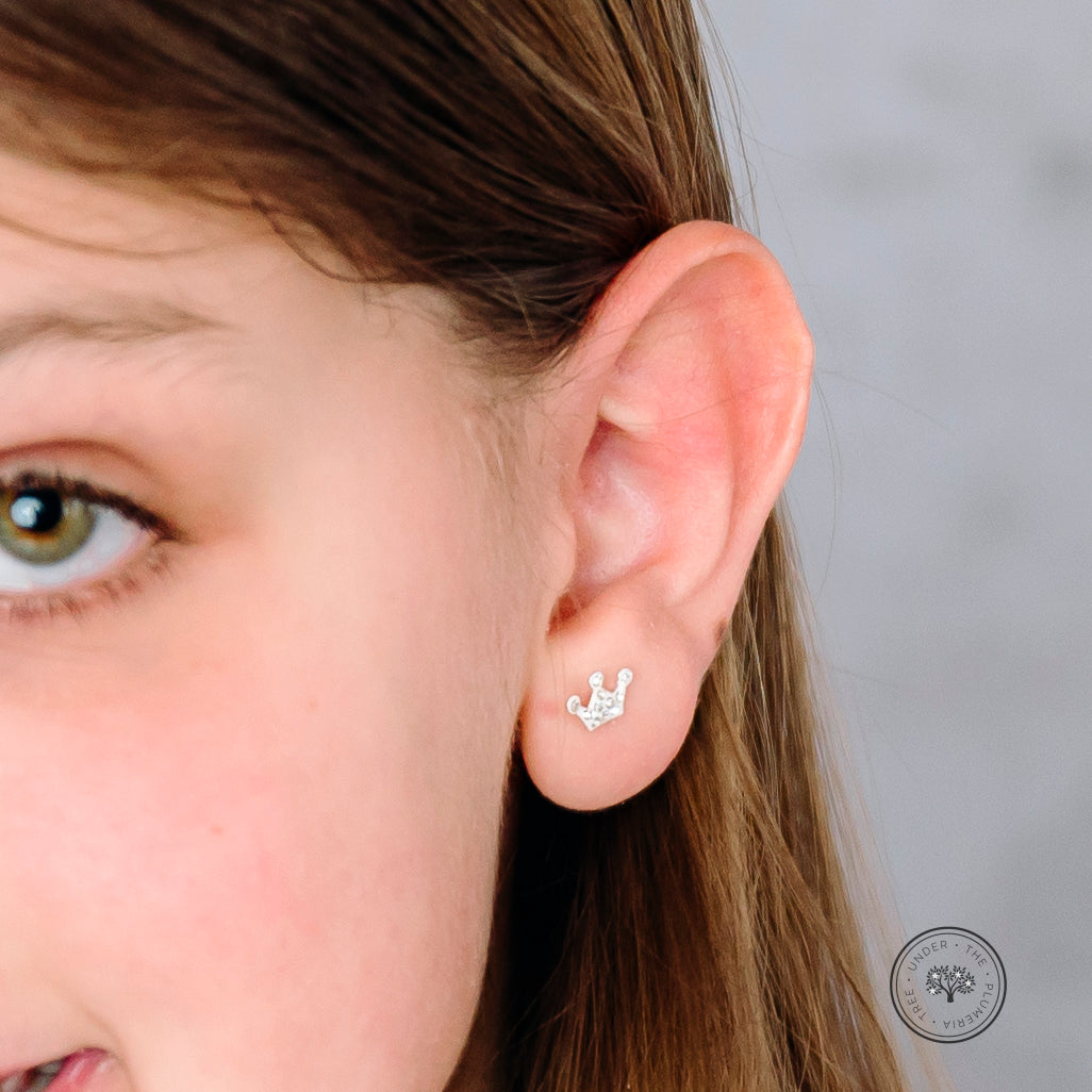 Silver sparkly crown earring shown on a young girl's ear so to understand the size of the earring.