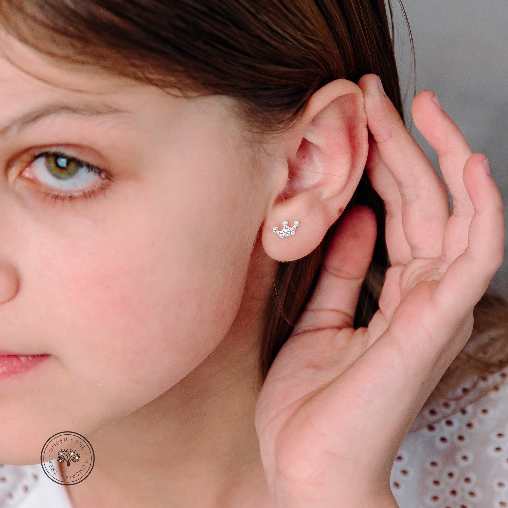 Youn girl showing her ear with white and silver crown kid's earring with sparkle jewels. 