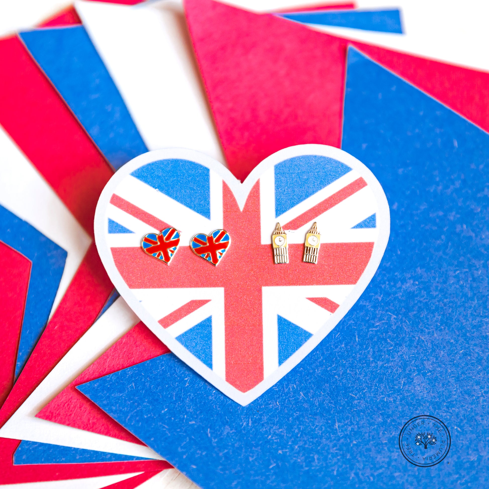 Red, White, and Blue banner cutouts as background for Great Britain heart shaped earring holder to rest on. Earrings include 2 pairs - 1 of the Union Jack in a heart shape and the other of clock towers that look like Big Ben. 